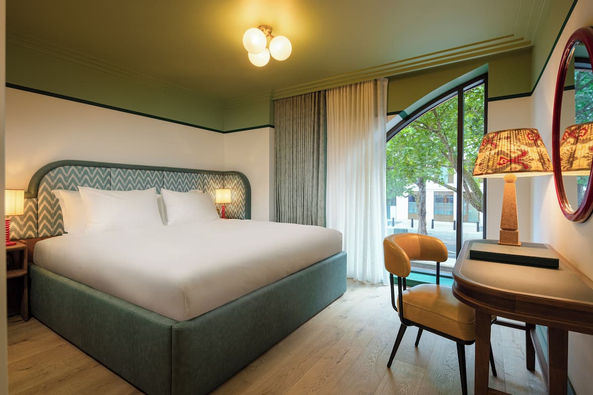 A hotel room with a large bed, a chair, a desk, and a window with curtains.