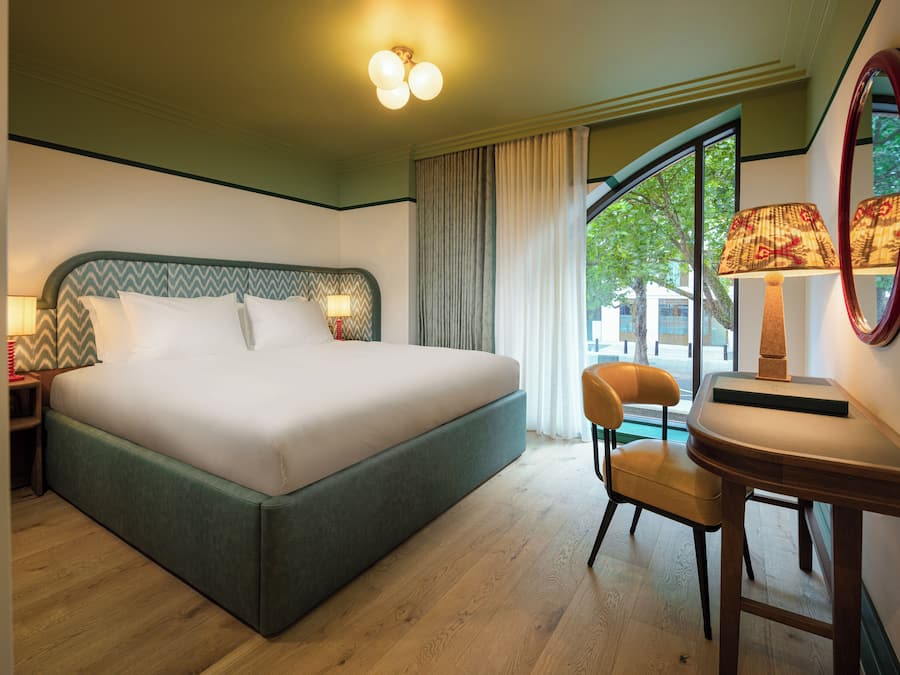 A hotel room with a large bed, a chair, a desk, and a window with curtains.