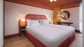 Ein Hotelzimmer mit einem großen Bett, zwei Nachttischen mit Lampen, einem runden Spiegel und einem kleinen Holztisch.