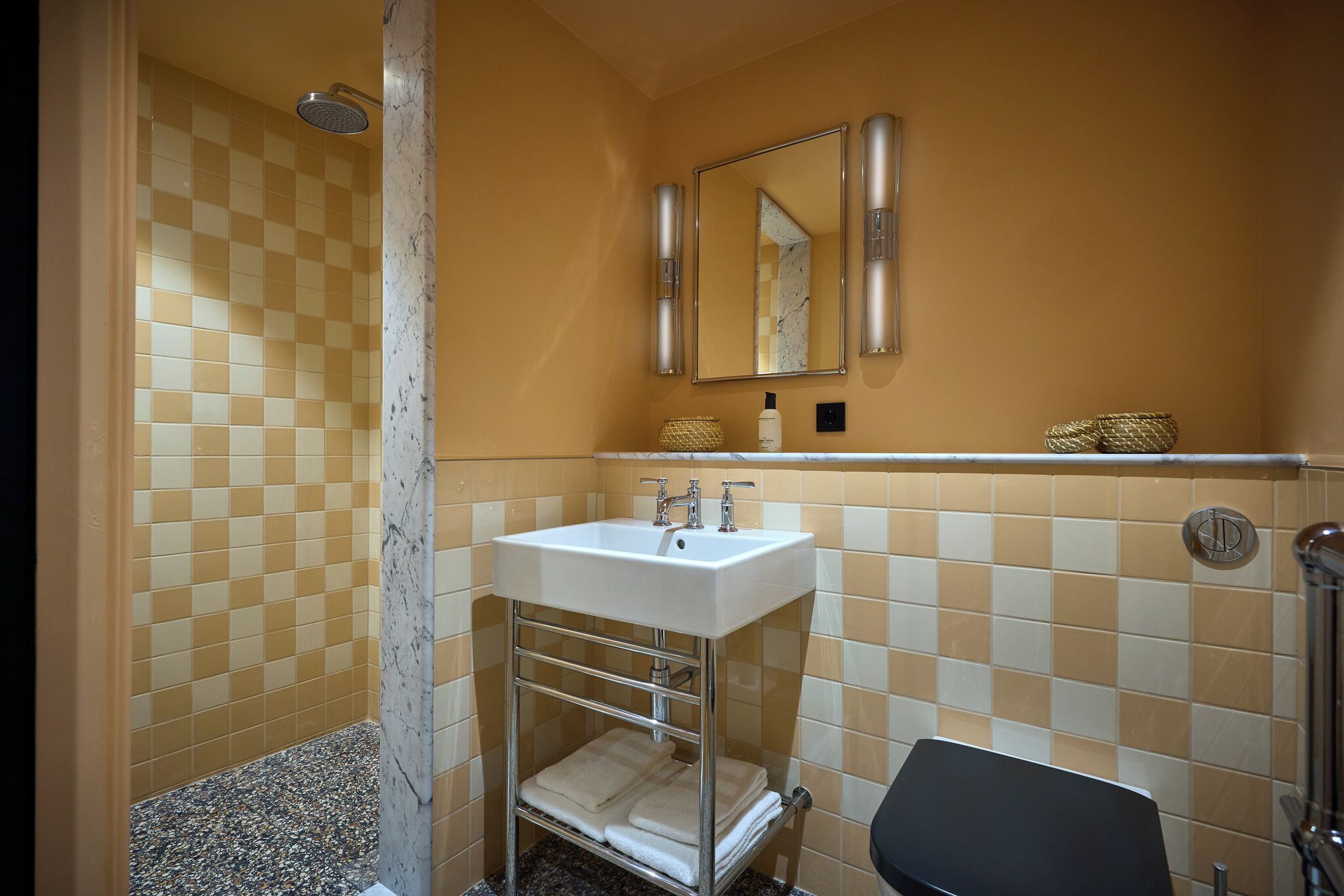 A bathroom with a checkered tile wall, a white sink with chrome fixtures, a mirror above the sink, and a towel rack with folded towels.