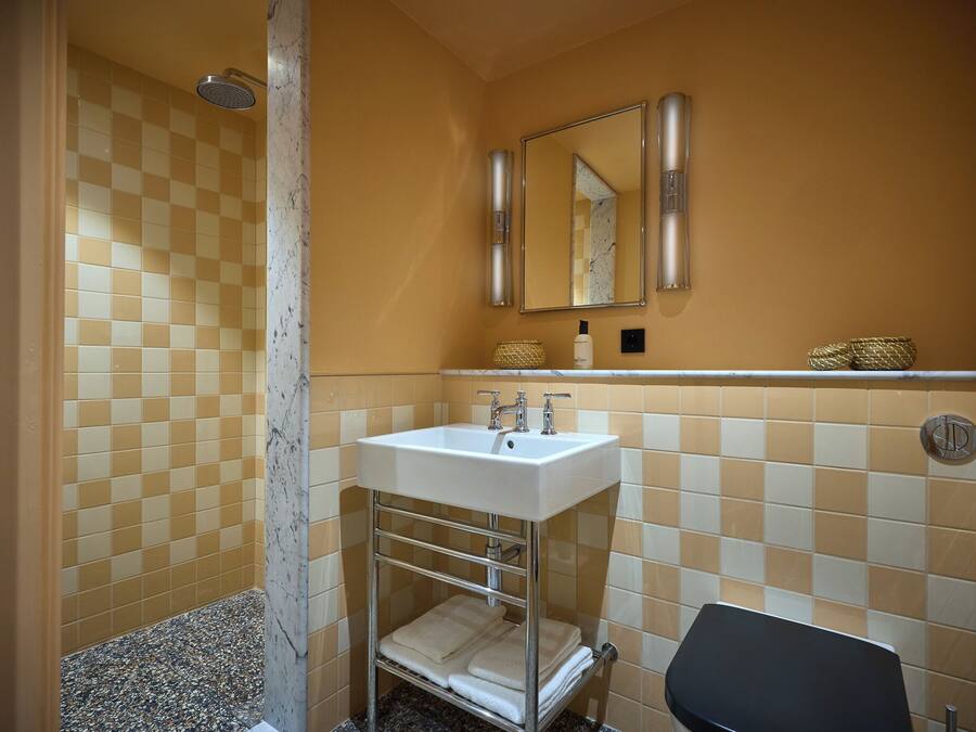 A bathroom with a checkered tile wall, a white sink with chrome fixtures, a mirror above the sink, and a towel rack with folded towels.