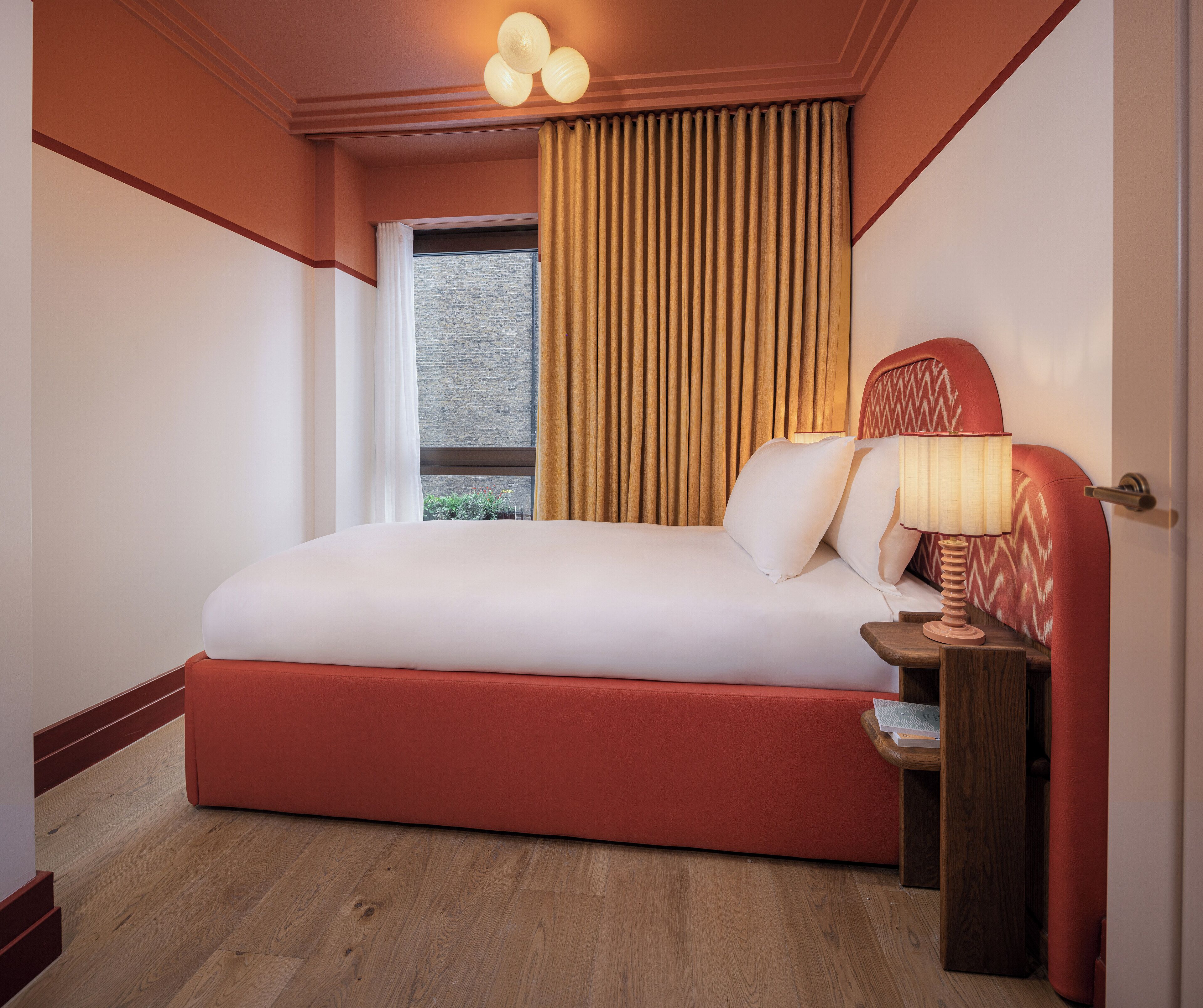 Ein Hotelzimmer mit einem großen Bett, einem Nachttisch aus Holz, einer Lampe und einem Fenster mit Vorhängen.