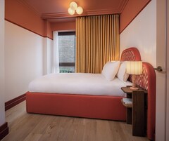 A hotel room with a large bed, a wooden nightstand, a lamp, and a window with curtains.