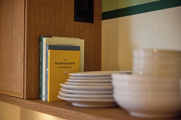 A stack of white plates on a wooden shelf next to a book titled 'The Hungry Chef'.