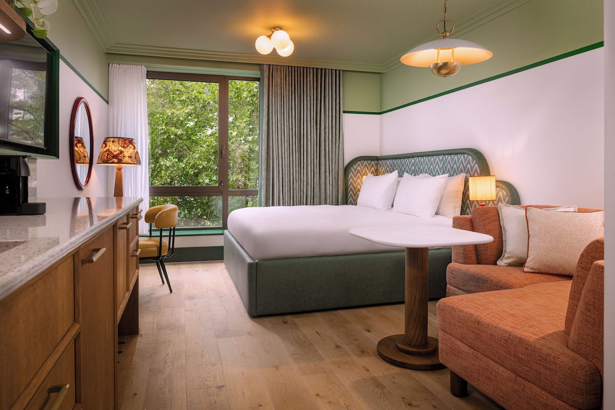 A hotel room with a bed, a sofa, a dining table, and a chair.