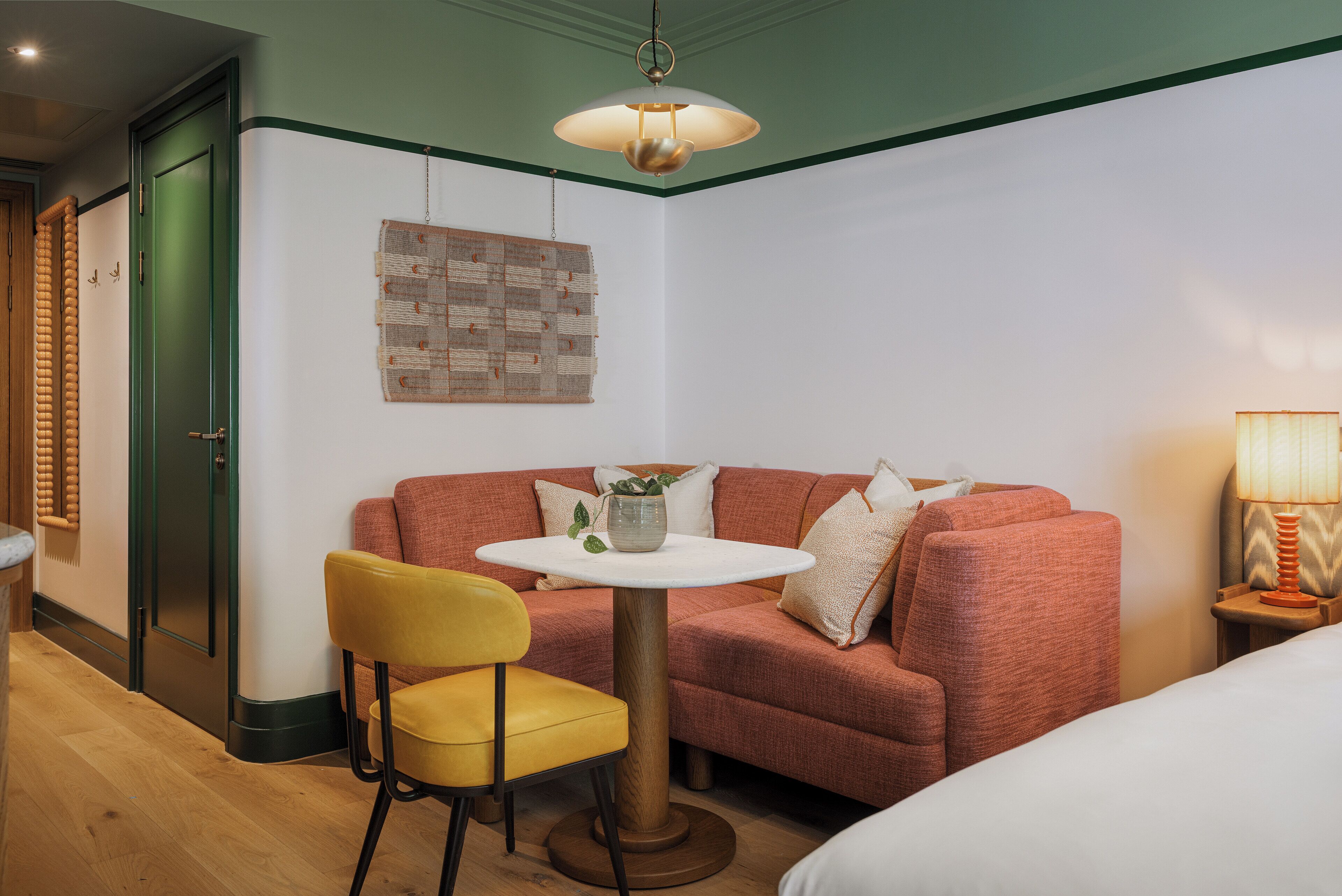 A room with a green door, a red sofa, a yellow chair, a round table, and a hanging light fixture.