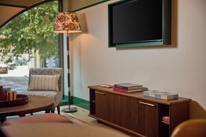 Une pièce chaleureuse avec une table ronde, un fauteuil à motifs, une lampe sur pied, une bibliothèque et un téléviseur fixé au mur.