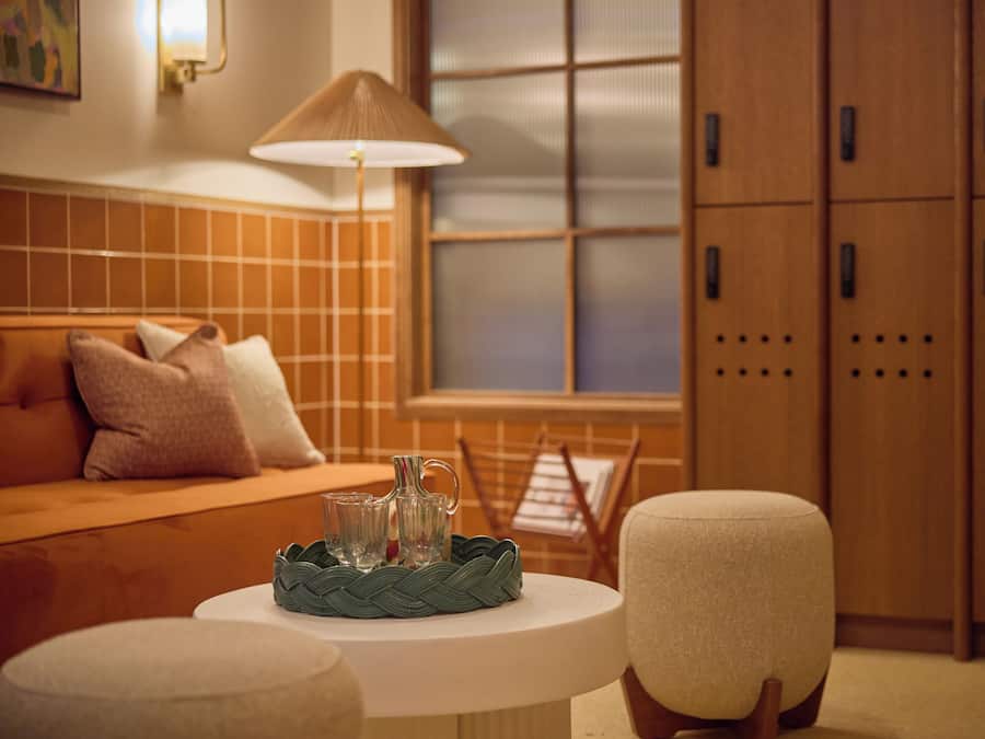 A cozy room with a sofa, a table with a lamp, and a window with blinds.