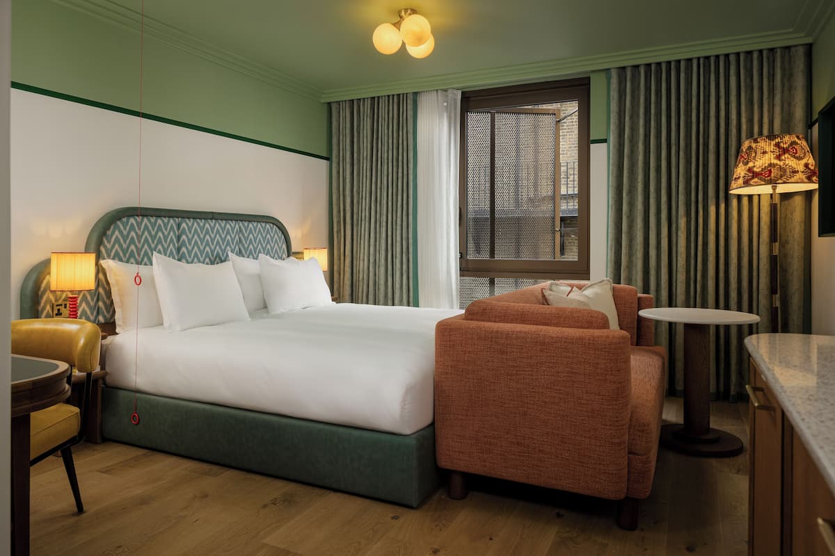 A hotel room with a bed, a sofa, a small table, and a lamp.