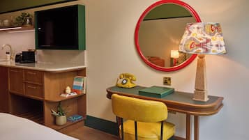 Ein Hotelzimmer mit Schreibtisch, Stuhl, Fernseher, Spiegel, Lampe und Telefon.