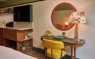 A hotel room with a desk, a chair, a television, a mirror, a lamp, and a telephone.