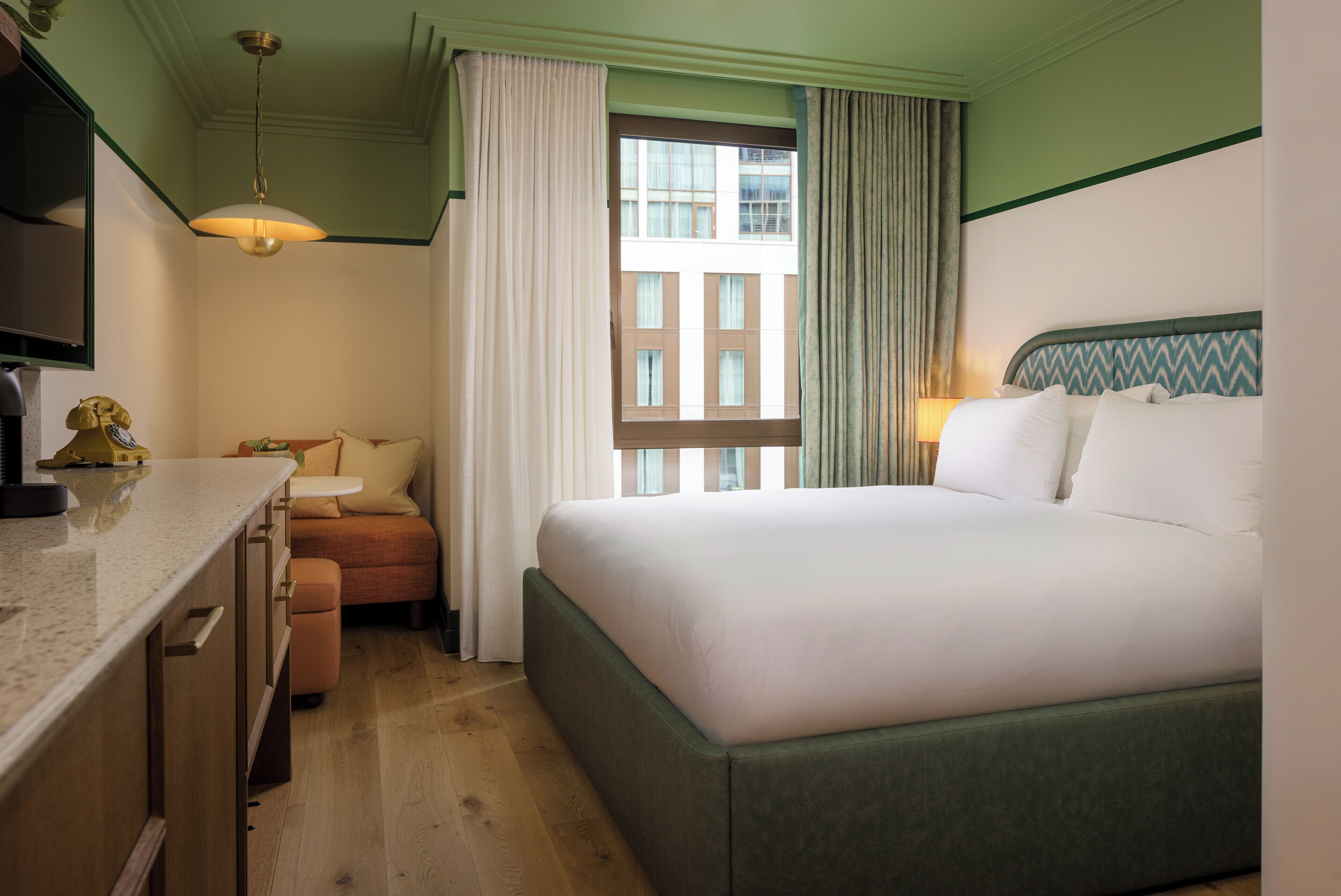 Quarto de hotel com cama, secretária, cadeira e janela com cortinas.