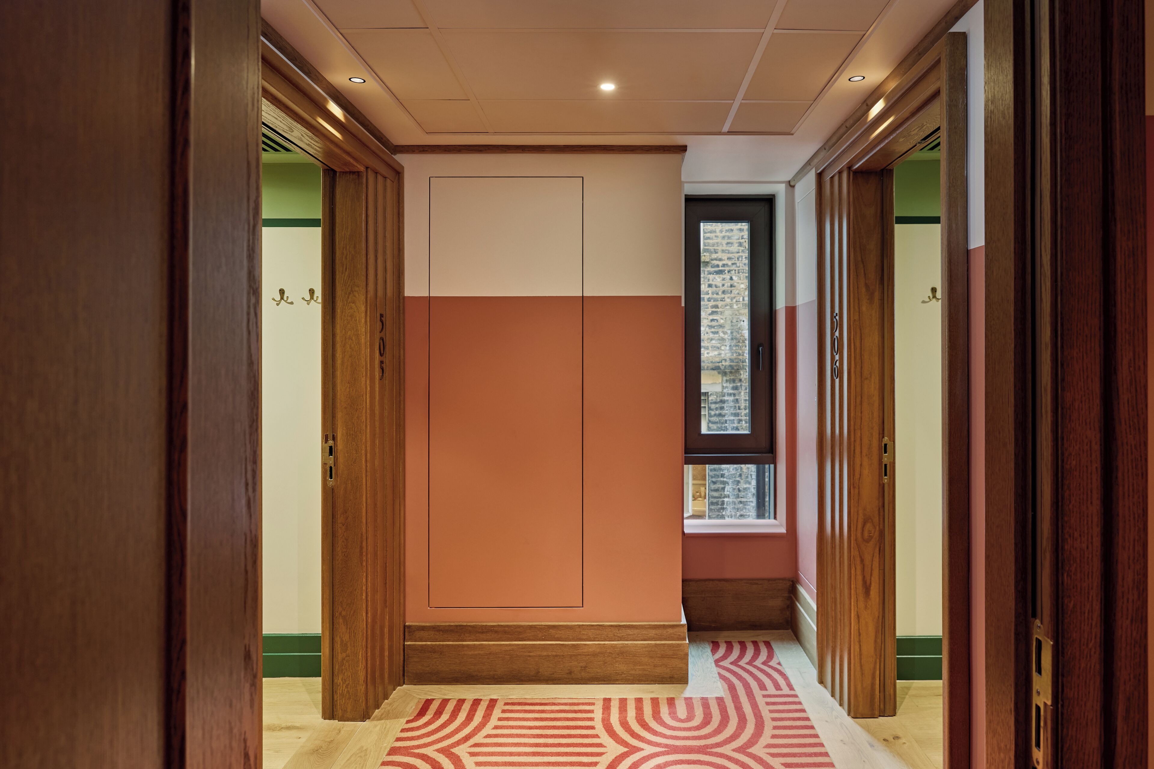 A hallway with wooden doors, a patterned carpet, and a window with a view.