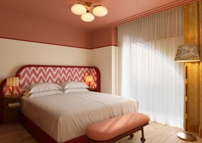 A neatly made bed with a red and white zigzag headboard, a bedside lamp, and a bench at the foot of the bed.