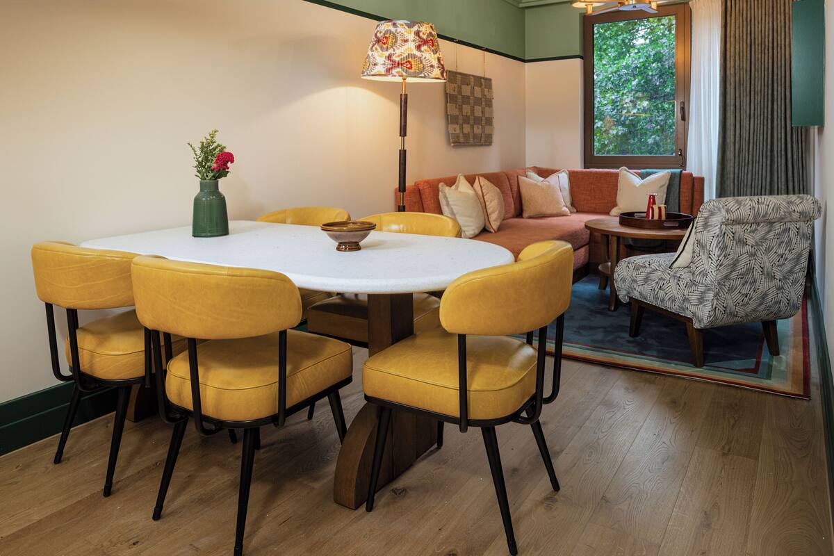 A dining area with a round table, yellow chairs, and a vase of flowers.