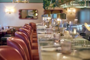 A restaurant with a long table set for dining, leather chairs, and a bar area with glasses and bottles.