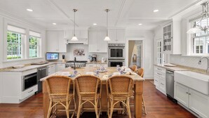 Une cuisine spacieuse avec des meubles blancs, un îlot central doté de chaises et une grande fenêtre.