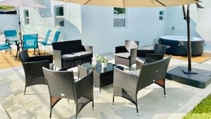 An outdoor patio with wicker furniture, a table, and a large umbrella. - Stylish House w Hot Tub Close to Beach Stadium (Oakland Park)