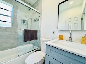 A modern bathroom with a glass-enclosed shower, a white toilet, a vanity with a mirror, and a towel hanging on a rack. - Modern 2-bedroom Retreat Near Beach Airport (Fort Lauderdale)