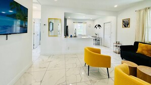 A modern living room with a large flat-screen TV, a yellow armchair, a black sofa with a yellow pillow, and a wooden coffee table. - Modern 2-bedroom Retreat Near Beach Airport (Fort Lauderdale)