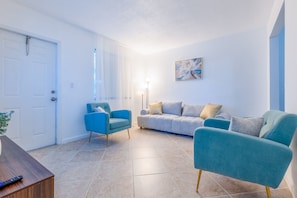Ein Wohnzimmer mit einer weißen Tür, einem blauen Sessel, einem grauen Sofa und einer Stehlampe.