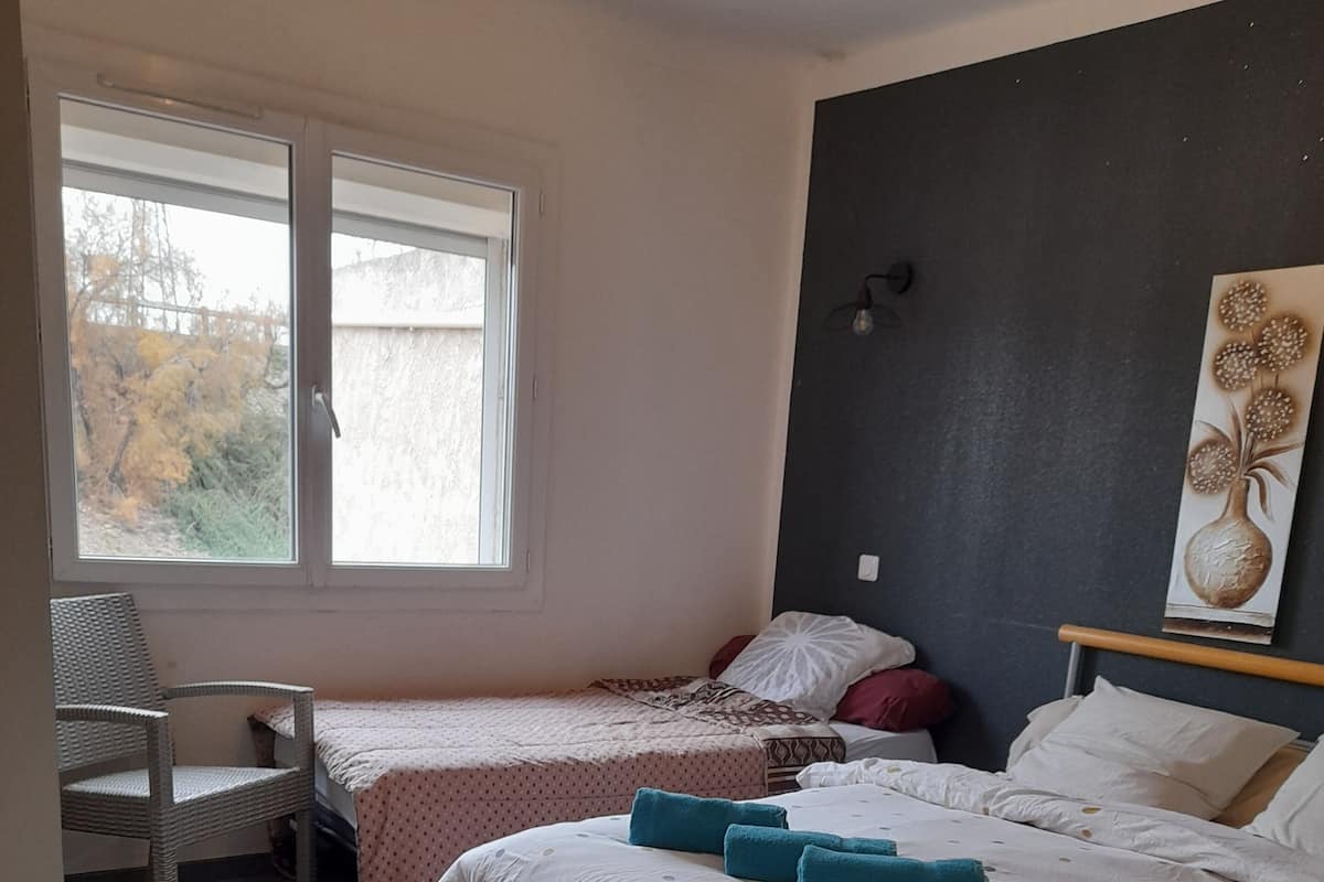 A bedroom with two beds, a chair, a window, and a wall-mounted light fixture.