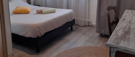 A bedroom with a bed, a bedside table, a chair, a round rug, and a window with curtains.