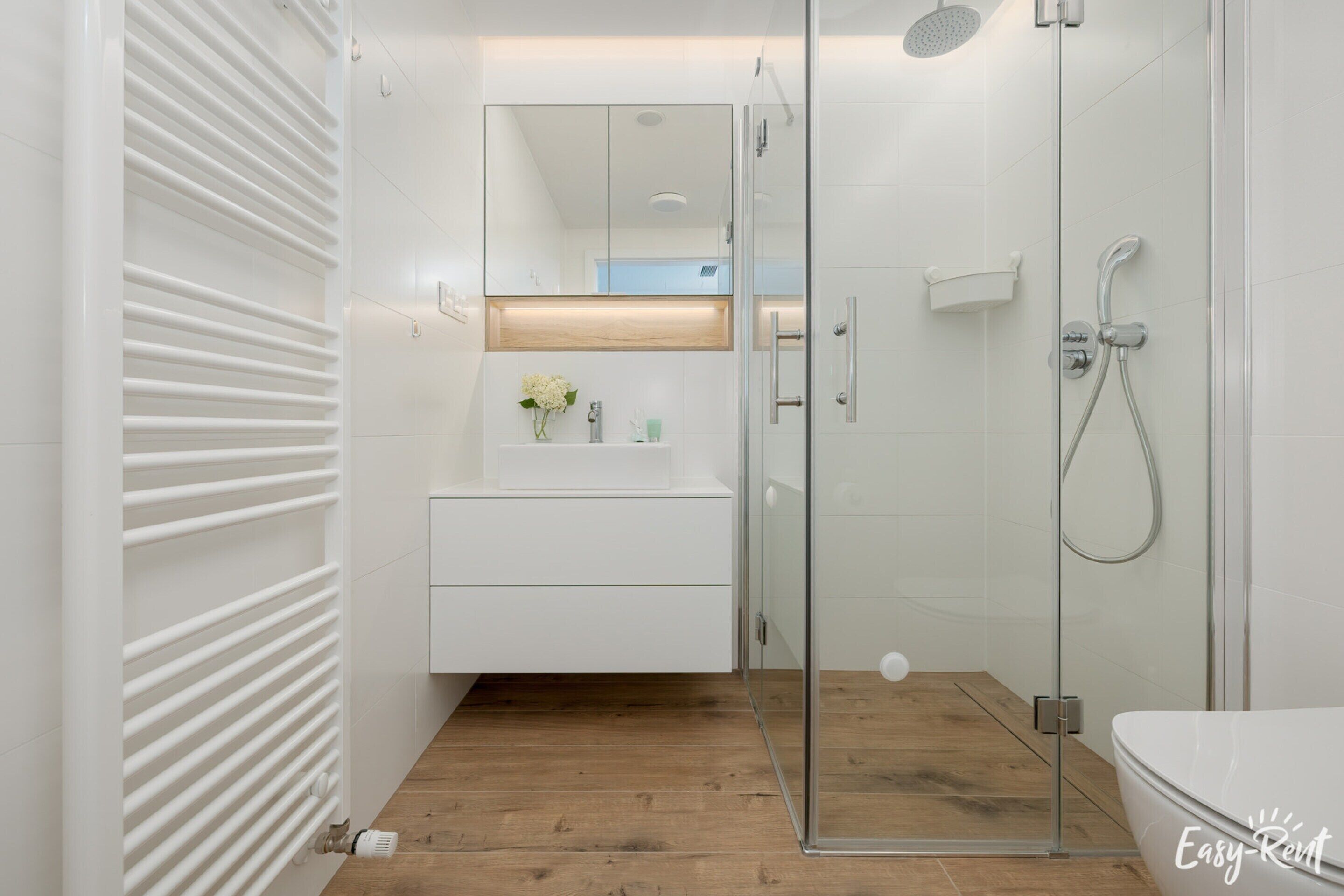 A modern bathroom with a glass shower enclosure, a white vanity with a mirror, and a wooden floor.