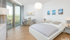 A modern bedroom with a large bed, a dining table, chairs, and a view through a sliding glass door. - Beachfront Holiday Apartment, Sauna, Swimming Pool (Rewal)
