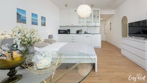 A modern bedroom with a glass coffee table, a bed, and a view of a kitchen with white cabinets and a hanging light fixture. - Beachfront Holiday Apartment, Sauna, Swimming Pool (Rewal)