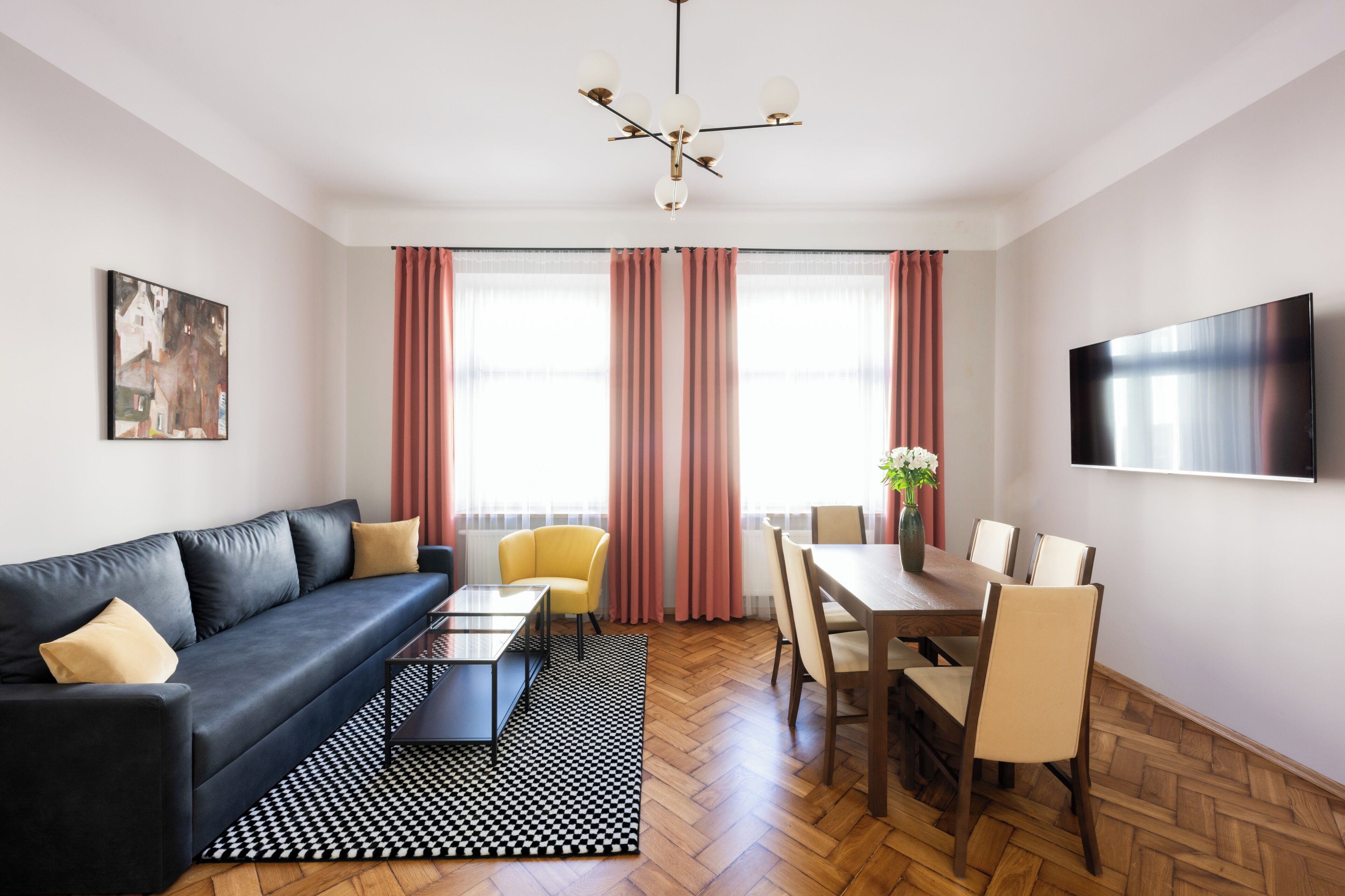 Ein modernes Wohnzimmer mit Sofa, Couchtisch, Esstisch und Stühlen. An der Wand ist ein Fernseher angebracht und ein Gemälde hängt dort.