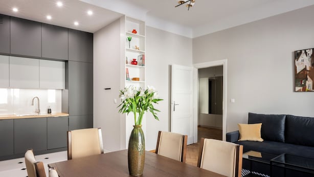 Un'elegante sala da pranzo moderna con tavolo in legno, sedie, un vaso con fiori e un lampadario.