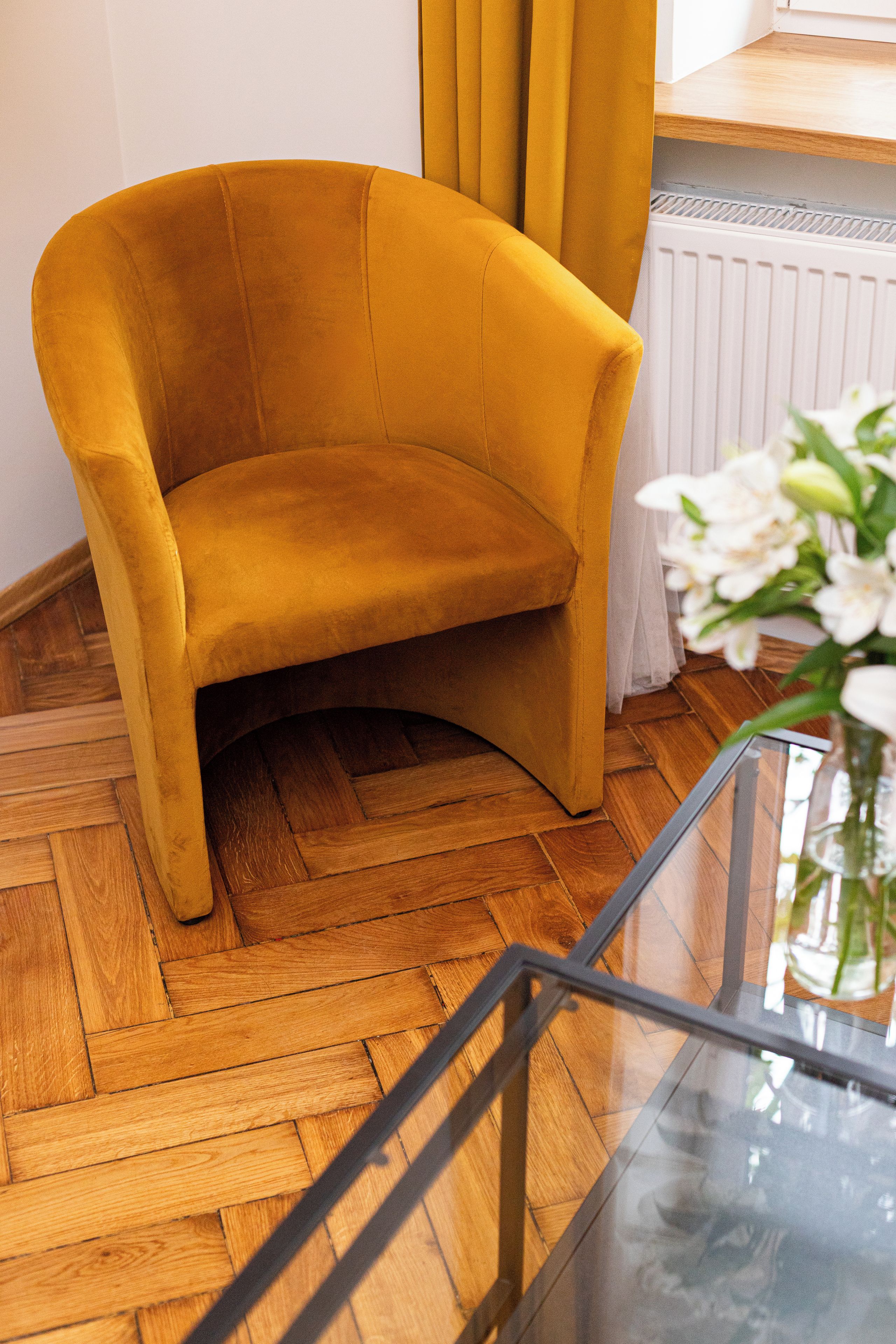A mustard-colored armchair in a room with wooden parquet flooring and a glass table.