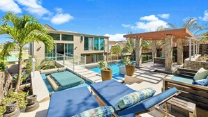 A modern pool area with lounge chairs and a pergola, surrounded by palm trees and a clear blue sky. - Villa Luana – Saltwater Pool Retreat with Mountain Views , Near Sandy Beach (Honolulu)