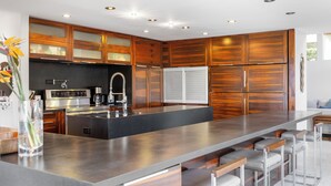 A modern kitchen with wooden cabinets, stainless steel appliances, and a large island with bar stools. - Villa Luana – Saltwater Pool Retreat with Mountain Views , Near Sandy Beach (Honolulu)