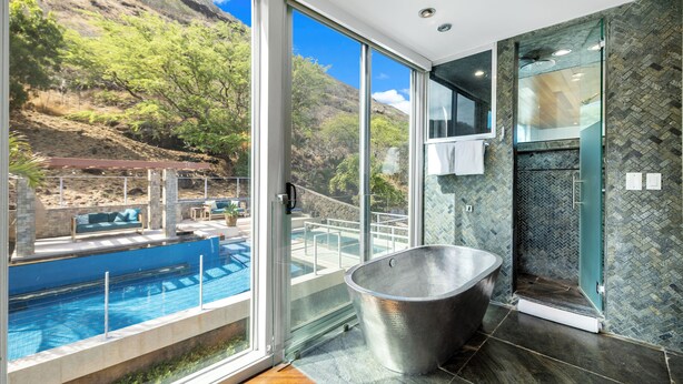 A modern bathroom with a large bathtub, a glass-enclosed shower, and a view of a pool and outdoor seating area. - Villa Luana – Saltwater Pool Retreat with Mountain Views , Near Sandy Beach (Honolulu)