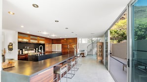 A modern kitchen with a large island, wooden cabinets, and a view of the outdoors. - Villa Luana – Saltwater Pool Retreat with Mountain Views , Near Sandy Beach (Honolulu)