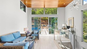 A modern living room with a sofa, armchairs, and a glass coffee table. A large window offers a view of a pool and outdoor area. - Villa Luana – Saltwater Pool Retreat with Mountain Views , Near Sandy Beach (Honolulu)
