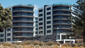 A modern multi-story building with a curved facade, located near a sandy beach with sparse vegetation. - Ocean Eleven Mt Maunganui (Mount Maunganui)