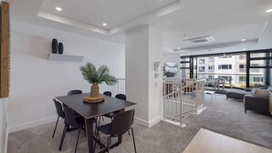 A modern living room with a dining area, large windows, and a staircase leading to an upper floor. - Ocean Eleven Mt Maunganui (Mount Maunganui)