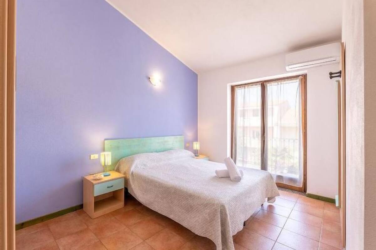 A bedroom with a bed, nightstands, a window, and an air conditioning unit.