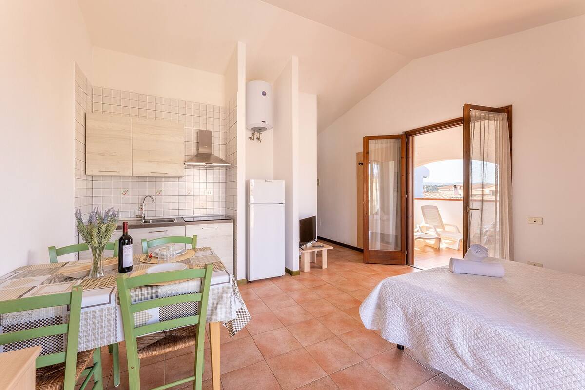 A compact room with a kitchen, dining area, and a bed.