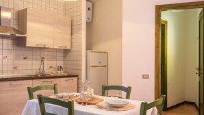 Un comedor con una mesa dispuesta para dos, una cocina con azulejos blancos y armarios de madera, y un refrigerador.