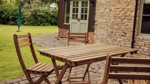 A wooden table and chairs set on a stone patio with a brick wall and a wooden door in the background. - The Falcon Cottages (Northampton)