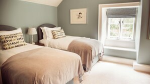 A bedroom with two beds, a window with a view, and a framed picture on the wall. - The Falcon Cottages (Northampton)