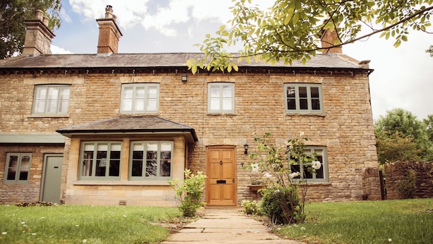 A stone house with a central wooden door, multiple windows, and a small garden. - The Falcon Cottages (Northampton)
