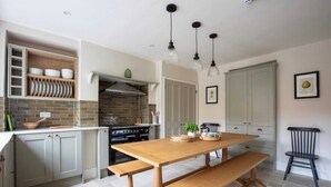 A kitchen with a wooden table, built-in shelves, a stove, and hanging pendant lights. - The Falcon Cottages (Northampton)