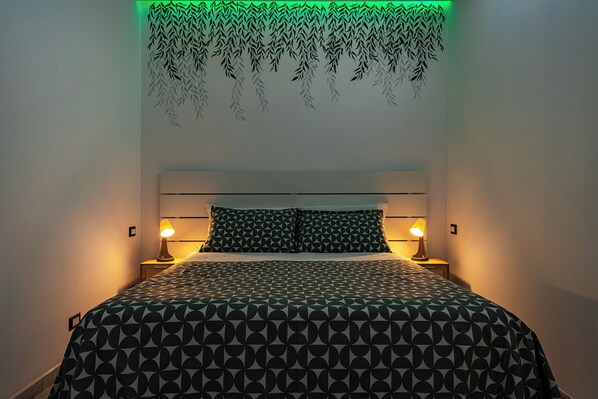 Una cama con una colcha de estampado geométrico, dos lámparas de noche y un aplique en la pared.