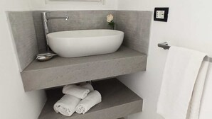 Un baño con un lavamanos grande blanco, un perchero y una sola flor blanca en la pared.