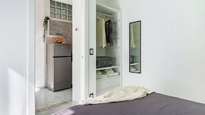 Un dormitorio con cama, armario, espejo y kitchenette con refrigerador.